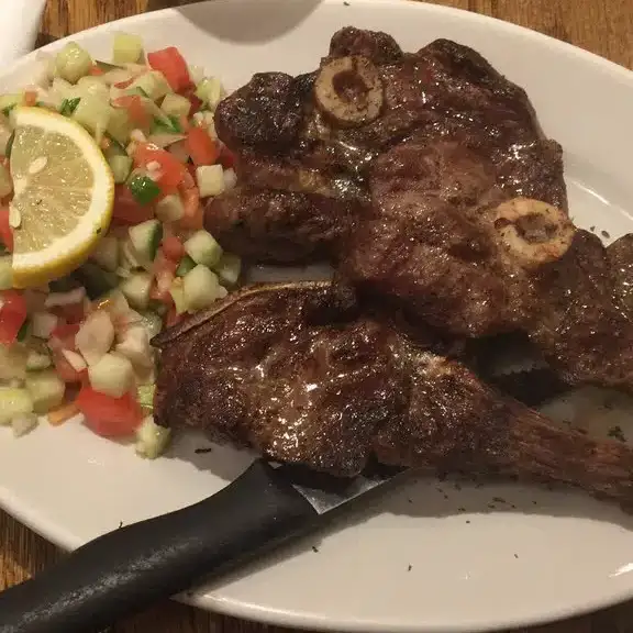 Juicy grilled lamb chops served with a side of fresh tomato cucumber salad and a lemon wedge