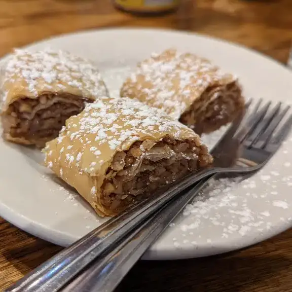 Sweet flaky baklava pastry rolls dusted with powdered sugar served on a plate with forks